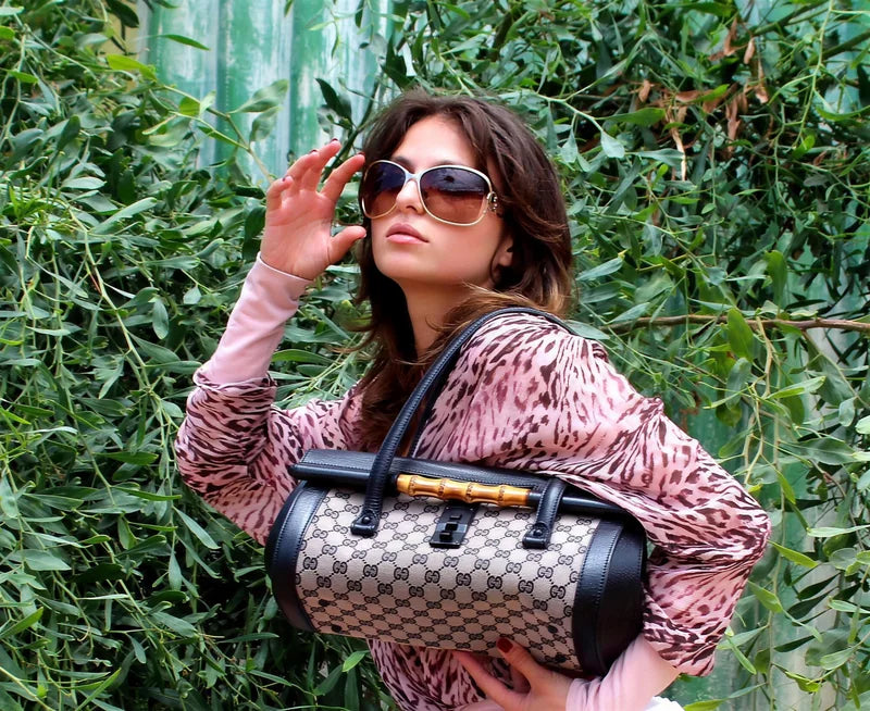 Model with oversized sunglasses holding the bamboo-handle bowler against a wall of foliage
