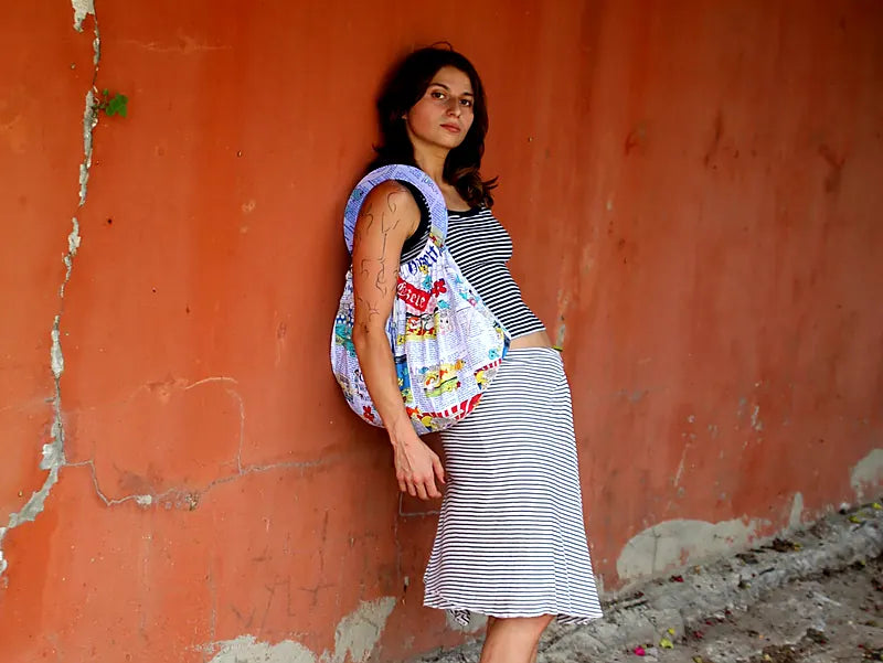 Model leaning on a terracotta wall wearing the gazette-print round-handle bag